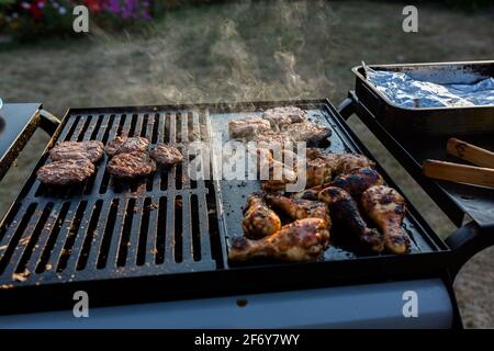 Nahaufnahme eines bbq-Grills mit Fleisch auf ihnen kochen, Sonneneinstrahlung im Hintergrund fängt den Rauch auf Stockfoto