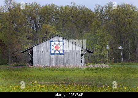 Eine alte Holzscheune entlang einer rustikalen Straße in Amerika ist mit einem traditionellen Quiltblock dekoriert Stockfoto