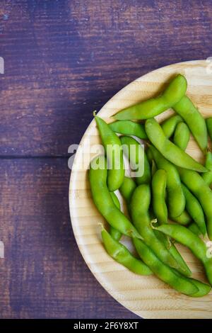 Eine Bambusplatte mit japanischen Edamame (Soja)-Bohnen auf einem rustikalen Holztisch. Stockfoto