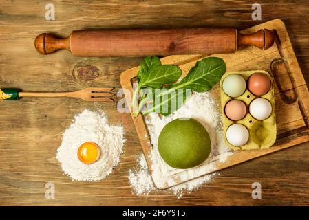 Grünes Teigbrötchen für die Herstellung von Nudeln, zubereitet auf dem Tisch mit Zutaten, traditionelle italienische Küche Stockfoto