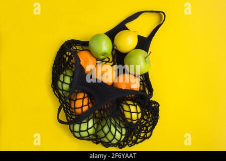Kein Plastikbeutel-Konzept. Mesh Shopping schwarze Tasche mit verschiedenen Früchten auf dem gelben Hintergrund Stockfoto