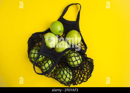 Kein Plastikbeutel-Konzept. Mesh Shopping schwarze Tasche mit grünen Äpfeln auf dem gelben Hintergrund Stockfoto