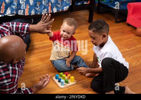 Brüder im Alter von 2 und 6 Jahren, die mit dem geometrischen Formsortierer spielen, Vater gab dem 2-Jährigen eine „hohe 5“ für den Erfolg Stockfoto