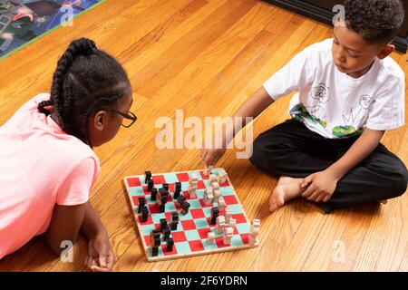 Das 11-jährige Mädchen spielt mit ihrem 6-jährigen Bruder Schach, spielt Spiel und lehrt ihn, wie man spielt Stockfoto