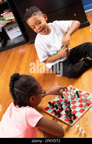 Das 11-jährige Mädchen spielt mit ihrem 6-jährigen Bruder Schach, spielt Spiel und lehrt ihn, wie man spielt Stockfoto