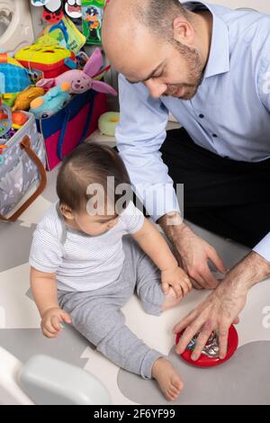 8 Monate alter Junge, vom Vater neues Spielzeug gezeigt, dreht oder dreht es so, dass sich die Perlen im Inneren bewegen Stockfoto