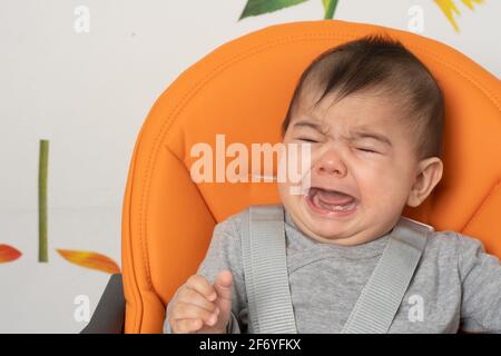 Sechs Monate alter Junge im Hochstuhl weinend, Nahaufnahme Stockfoto