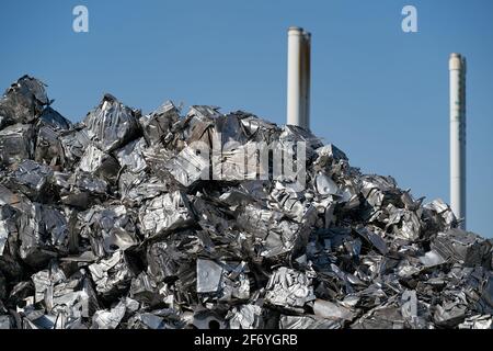 Würfel von gepresstem Schrott auf einem Schrottplatz im Hafen in Magdeburg in Deutschland im Hintergrund Schornsteine von Ein Industriegebiet Stockfoto