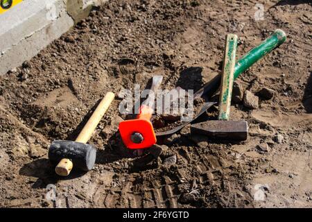 Unschärfe-Hammer, Hammer, Meißel und Bajonett der Schaufel liegen auf dem Boden. Set von Werkzeugen für die Verlegung von Pflastersteinen. Arbeitsprozess. Vorbereitung zum Lay y Stockfoto