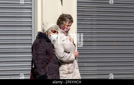 Dundee, Tayside, Schottland, Großbritannien. April 2021. UK Wetter: Frühlingssonne mit einer kühlen Brise durch Nordostschottland mit Temperaturen bis zu 12 Grad Die Menschen verbringen immer noch Zeit im Freien, um in Dundee City Kontakte zu knüpfen, da viele Geschäfte in der Tayside-Region während der Covid-19-Sperre auf Level 4 noch geschlossen sind. Zwei ältere Frauen sind sich der sozialen Distanzierungsrichtlinien und des Tragens von Gesichtsmasken bewusst, die draußen gemeinsam das sonnige Wetter im Stadtzentrum genießen. Kredit: Dundee Photographics/Alamy Live Nachrichten Stockfoto