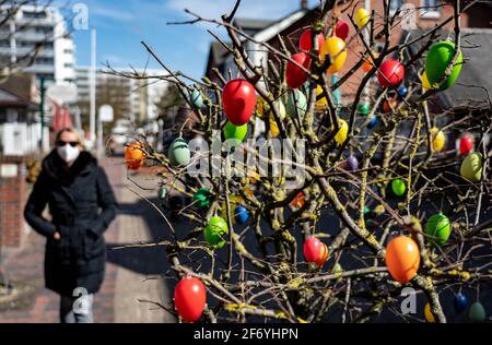 03. April 2021, Schleswig-Holstein, Westerland/Sylt: Eine Frau mit Mundnasenschutz geht im Zentrum von Westerland an einem Busch mit Ostereiern vorbei. Foto: Axel Heimken/dpa Stockfoto