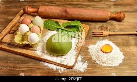 Grünes Teigbrötchen für die Herstellung von Nudeln, zubereitet auf dem Tisch mit Zutaten, traditionelle italienische Küche Stockfoto