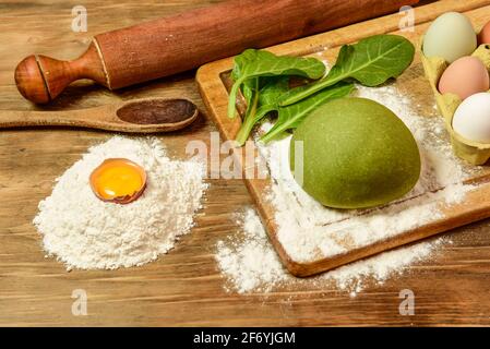 Grünes Teigbrötchen für die Herstellung von Nudeln, zubereitet auf dem Tisch mit Zutaten, traditionelle italienische Küche Stockfoto