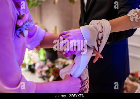 Die Hände der Braut und des Bräutigams sind mit einem bestickten Handtuch gebunden. Ukrainische Hochzeitstraditionen Stockfoto