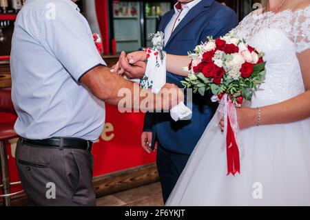 Die Hände der Braut und des Bräutigams sind mit einem bestickten Handtuch gebunden. Ukrainische Hochzeitstraditionen Stockfoto