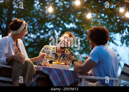 Gruppe multiethnischer Freunde, die lachen, reden und am Tisch im Freien sitzen Stockfoto