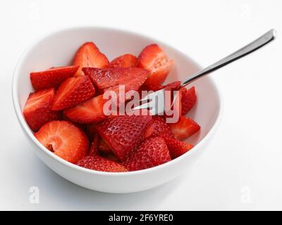 Weiße Schüssel voll von geschnittenen Erdbeeren mit Gabel auf weiß Hintergrund Stockfoto