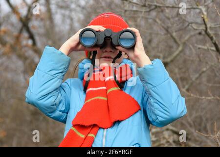 Ein Mädchen schaut durch ein Fernglas auf einem Hintergrund eines Winterwaldes, Vorderansicht, Nahaufnahme Stockfoto