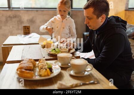 Die Familie frühstückte morgens in der Cafeteria. Vollkornwaffeln, Eis, Kiwi und Kaffee auf braunem rustikalem Holztisch. Stockfoto