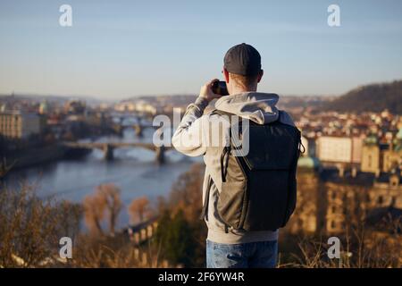 Mann fotografiert die Skyline der Stadt. Rückansicht des Reisenden vor dem Stadtbild mit der Karlsbrücke, Prag, Tschechische Republik. Stockfoto