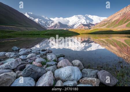 Lenin Peak Bergmassiv vom Achik-Tash Basislager aus gesehen mit Gletscherlagune, Felsen und Reflexion an der Grenze zwischen Kirgisistan und Tadschikistan Stockfoto