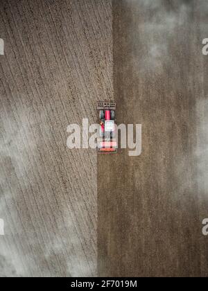 Roter Traktor pflügt Feld Luftaufnahme von oben durch Wolken. Drohnen Anbau Maschine Ausrüstung arbeiten Pflügen Land Stockfoto