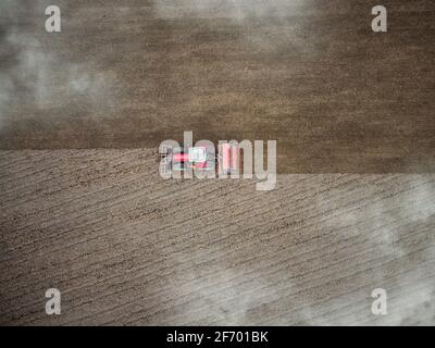 Roter Traktor pflügt Feld Luftaufnahme von oben durch Wolken. Drohnen Anbau Maschine Ausrüstung arbeiten Pflügen Land Stockfoto
