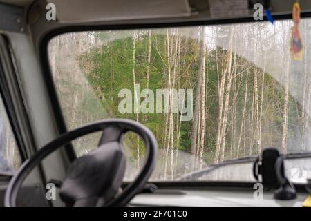 Der Blick vom Auto durch die schmutzige Windschutzscheibe des Waldes. Blick vom Fahrersitz des Staplers. Stockfoto