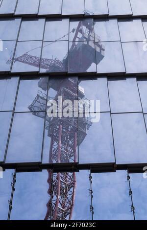 Sehr hoher Hebekran, der für den Bau von Wolkenkratzern verwendet wird, die sich darin spiegeln Die Glas- und Metallwände eines Wolkenkratzers Stockfoto