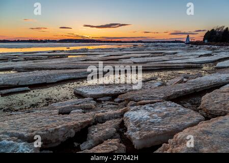 Gefrorenes Meer mit schwimmenden Eisblöcken gegen einen entfernten rot-weißen Leuchtturm während des Sonnenuntergangs in Charlottetown Prince Edward Island, Kanada Stockfoto