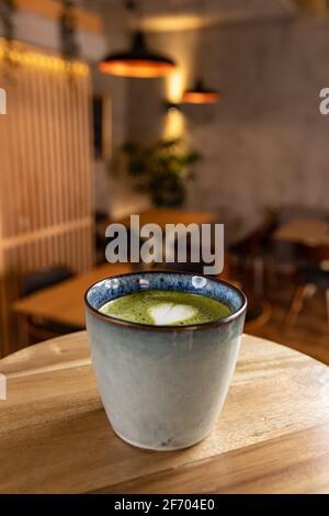 Eine Tasse Matcha Latte auf dem Tisch verwischen die Inneneinrichtung des Restaurantcafés Hintergrund Stockfoto