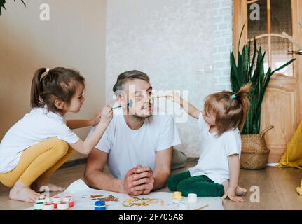 Kinder haben Spaß mit ihrem Vater. Mädchen zeichnen mit bunten Farben auf die Haut eines Mannes. Kreativität und Fantasie. Vatertag und der Co Stockfoto