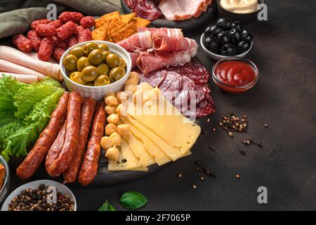 Würste verschiedener Art, geräuchertes Fleisch, Käse und Oliven auf braunem Hintergrund mit Platz zum Kopieren. Charcuterie-Board. Stockfoto