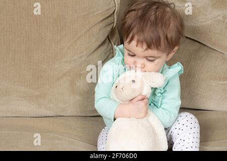 10 Monate altes Baby Mädchen umarmt Lieblings ausgestopftes Tier Lamm Spielzeug Stockfoto