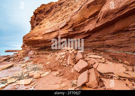 Am Cavendish Beach, auf Kanadas Prince Edward Island, ist der flache rote und türkisfarbene Sandstein mit gefallenen Steinen bedeckt, die durch Erosion verursacht wurden Stockfoto