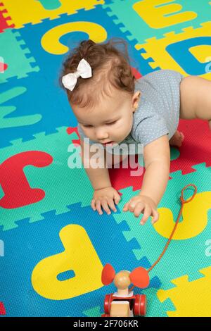 7 Monate altes Mädchen kriecht auf Spielzeug zu und greift nach Spielzeug Stockfoto