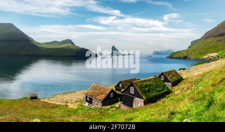 Malerischer Blick auf die mit Gras bewachsenen, tradicional faroese Häuser im Dorf Bour. Drangarnir und Tindholmur Meer Stapel auf dem Hintergrund. Vagar Island, Fa Stockfoto