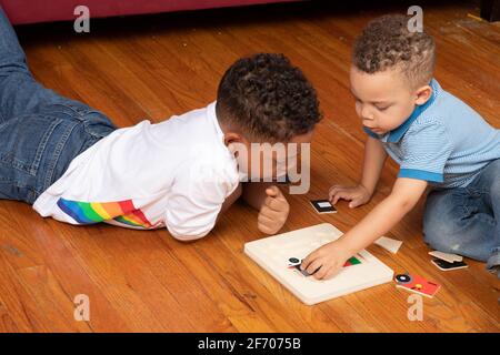 3-jähriger Junge, der Peg Puzzle macht, beobachtet und von einem 7-jährigen Bruder unterstützt Stockfoto