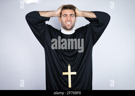 Junger hispanischer Mann in Priesteruniform, der auf weißem Hintergrund steht Leiden unter Kopfschmerzen verzweifelt und gestresst, weil Schmerzen und Migräne Mit Stockfoto