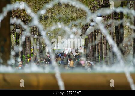 Blick hinter die Wasserstrahlen von einem Brunnen in Ein Park voller Menschen mit Masken zu Fuß Stockfoto