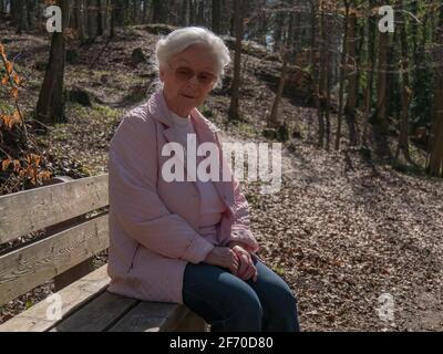 Ältere Frau, die allein auf der Parkbank sitzt Stockfoto