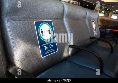 Perspektivische Ansicht leerer Sitze im Flughafen mit sozial distanzierenden Regulierungszeichen für COVID-19-Epidemien. Selektiver Fokus. Stockfoto