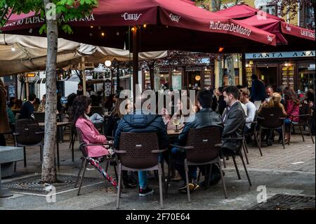 Madrid, Spanien. April 2021. Die Menschen sitzen auf einer Terrasse auf dem Santa Ana Platz in der Innenstadt von Madrid. Die Polizei kontrolliert den Zustrom von Menschen in der Innenstadt von Madrid als sanitäre Maßnahme, um Coronavirus-Infektionen während der Osterferien zu verhindern. Quelle: Marcos del Mazo/Alamy Live News Stockfoto