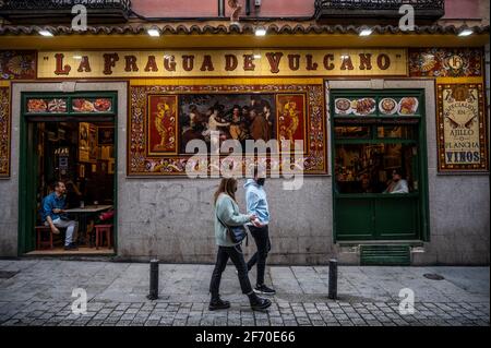 Madrid, Spanien. April 2021. Ein Paar, das Gesichtsmasken trägt, um die Ausbreitung des Coronavirus zu stoppen, geht an einer typischen spanischen Taverne in der Innenstadt von Madrid vorbei. Die Polizei kontrolliert den Zustrom von Menschen in der Innenstadt von Madrid als sanitäre Maßnahme, um Coronavirus-Infektionen während der Osterferien zu verhindern. Quelle: Marcos del Mazo/Alamy Live News Stockfoto