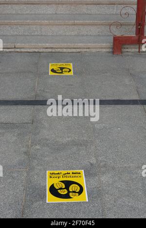 Ein Bodenschild in Arabisch und Englisch, das ein setzt Markieren Sie die Position, um Abstand und Abstand zwischen beiden zu halten Menschen während der weltweiten Pandemie von covid-19 Stockfoto