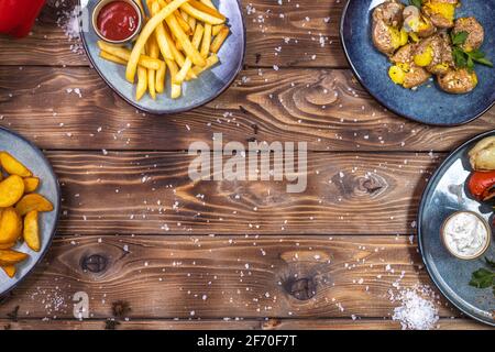Flaches Layout aus gekochten Kartoffeln, Pommes frites, Paprika, grobem Salz, gegrilltem Gemüse auf braunem Holzhintergrund. Speicherplatz kopieren. Stockfoto