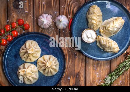 Khinkali und Manti mit Fleisch auf einem Teller auf einem braunen Holzboden, verziert mit Rosmarin, Knoblauch, Gewürzen und Kirschtomaten. Speisekarte im Restaurant. Stockfoto