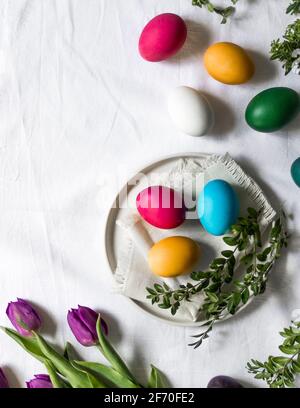 Osterszene - bemalte Eier liegen auf Tischdecke, auf dem Küchentisch neben frischen lila Tulpen, bereit, in den Osterkorb gelegt werden. Stockfoto