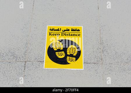 Ein Bodenschild in Arabisch und Englisch, das ein setzt Markieren Sie die Position, um Abstand und Abstand zwischen beiden zu halten Menschen während der weltweiten Pandemie von covid-19 Stockfoto