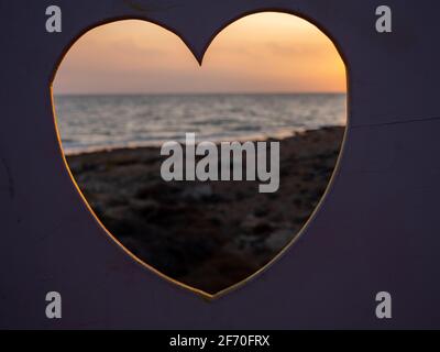 Blick durch das Loch in Form eines Herzens über einen wunderschönen Sonnenuntergang an der Mittelmeerküste. Liebe, Fürsorge und Valentinstag romantische Konzept. Stockfoto
